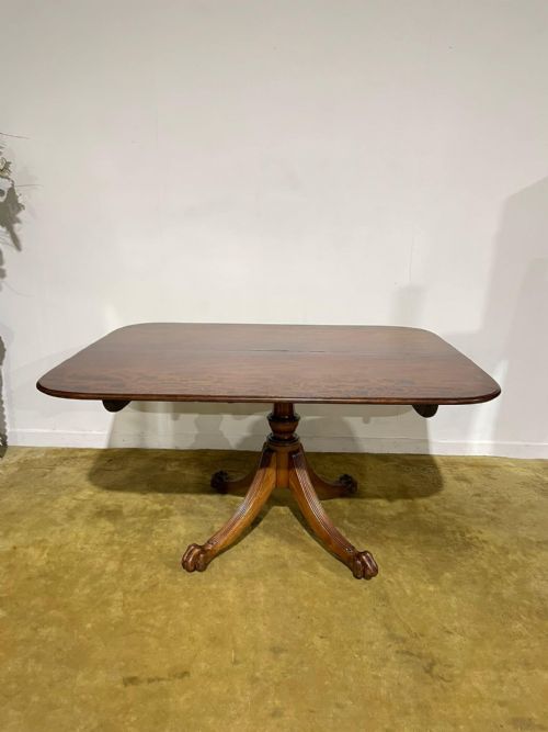 fig 1. A late Regency mahogany tilt-top breakfast table featuring a rectangular polished top with rounded corners, supported by a central pedestal and reeded quadruped legs with brass paw feet.