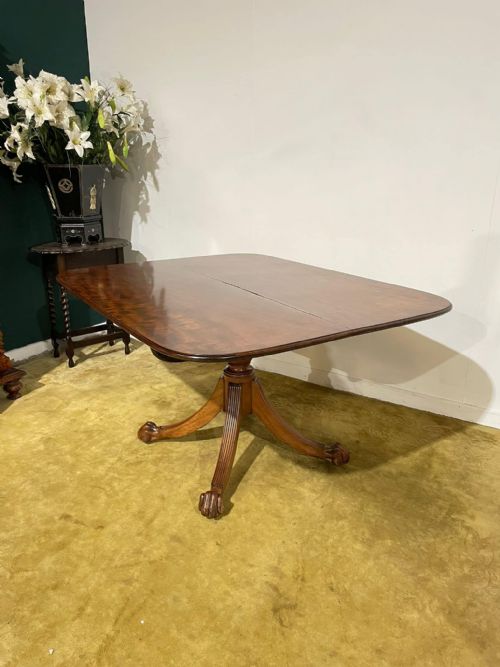 fig 2. A late Regency mahogany tilt-top breakfast table featuring a rectangular polished top with rounded corners, supported by a central pedestal and reeded quadruped legs with brass paw feet.