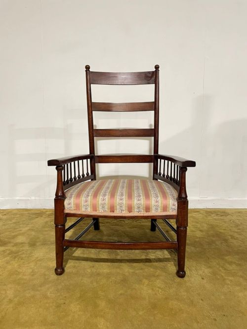 fig 1. An Arts and Crafts dark beech ladder back armchair featuring turned spindle arm supports, top finials, and a striped fabric upholstered seat.