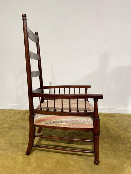 fig 2. An Arts and Crafts dark beech ladder back armchair featuring turned spindle arm supports, top finials, and a striped fabric upholstered seat.