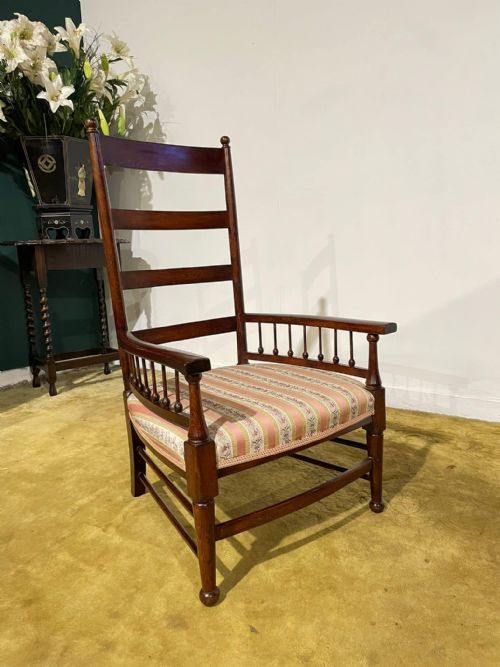 fig 3. An Arts and Crafts dark beech ladder back armchair featuring turned spindle arm supports, top finials, and a striped fabric upholstered seat.