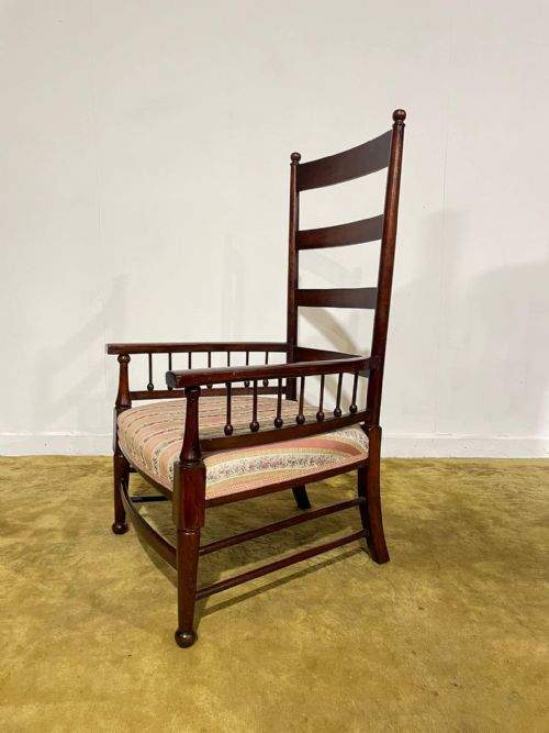 fig 4. An Arts and Crafts dark beech ladder back armchair featuring turned spindle arm supports, top finials, and a striped fabric upholstered seat.