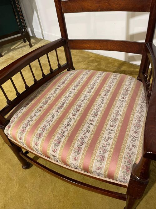 fig 6. An Arts and Crafts dark beech ladder back armchair featuring turned spindle arm supports, top finials, and a striped fabric upholstered seat.
