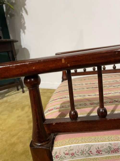 fig 7. An Arts and Crafts dark beech ladder back armchair featuring turned spindle arm supports, top finials, and a striped fabric upholstered seat.