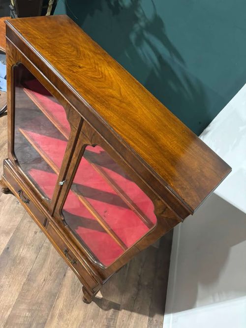 fig 3. A 1930s walnut display cabinet featuring two glazed doors with arched upper panels, red fabric-lined shelves, two lower drawers, and cabriole legs.