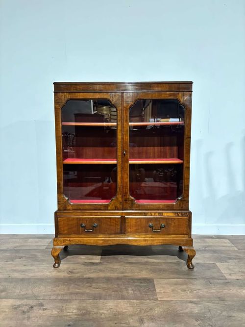 fig 4. A 1930s walnut display cabinet featuring two glazed doors with arched upper panels, red fabric-lined shelves, two lower drawers, and cabriole legs.