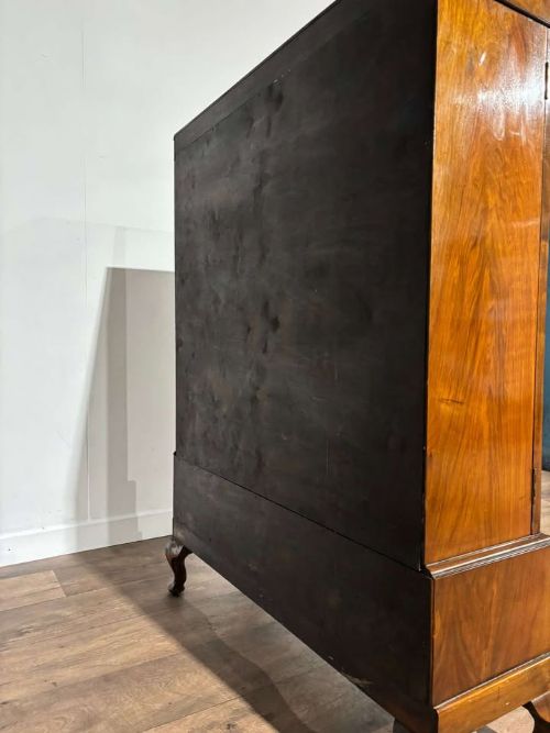 fig 6. A 1930s walnut display cabinet featuring two glazed doors with arched upper panels, red fabric-lined shelves, two lower drawers, and cabriole legs.