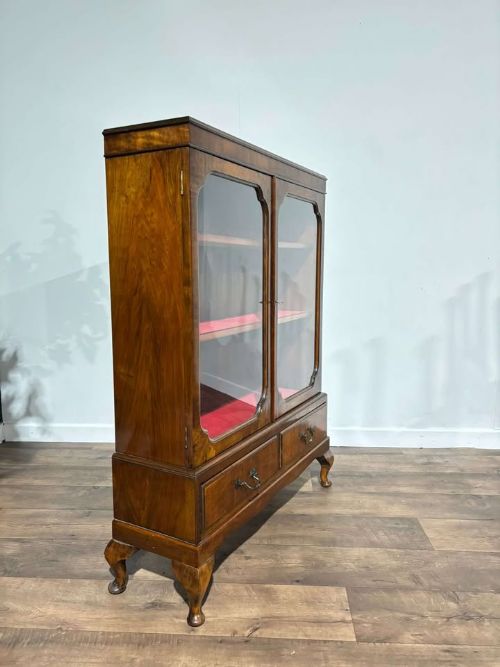fig 7. A 1930s walnut display cabinet featuring two glazed doors with arched upper panels, red fabric-lined shelves, two lower drawers, and cabriole legs.