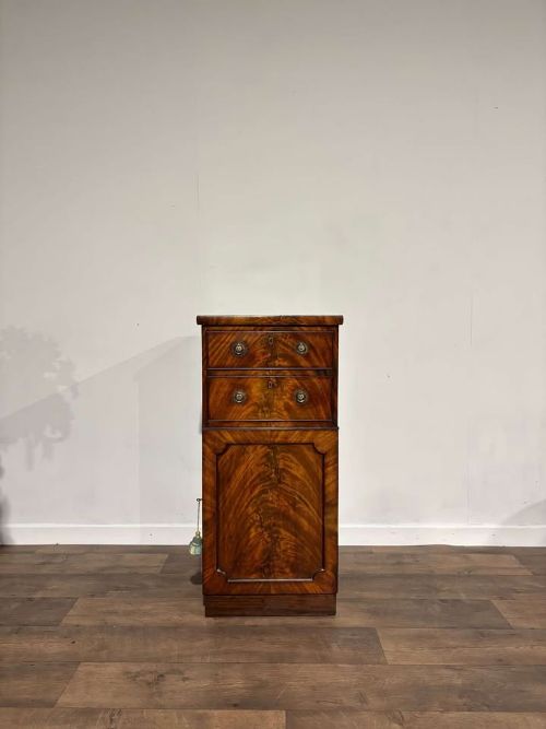 fig 2. A tall Victorian flame mahogany cabinet featuring two upper drawers with brass ring handles above a single panelled cupboard door on a plinth base.