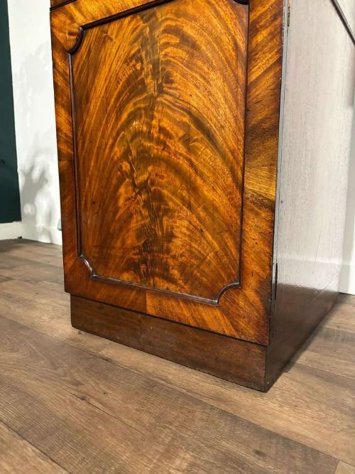 fig 7. A tall Victorian flame mahogany cabinet featuring two upper drawers with brass ring handles above a single panelled cupboard door on a plinth base.