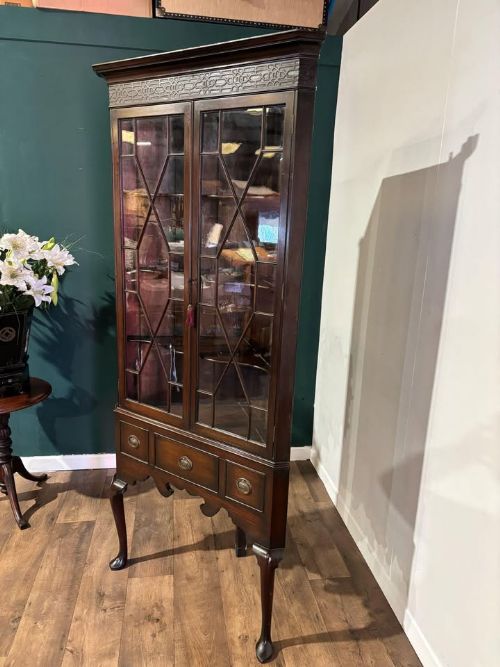 fig 1. A tall mahogany corner display cabinet featuring astragal glazed doors, a fretwork frieze, and elevated on cabriole legs.