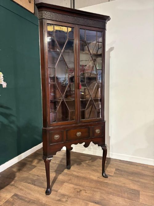 fig 2. A tall mahogany corner display cabinet featuring astragal glazed doors, a fretwork frieze, and elevated on cabriole legs.