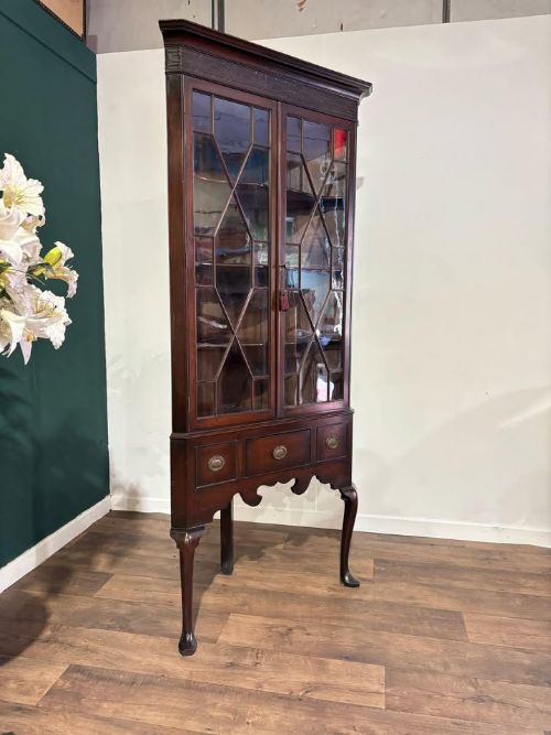 fig 3. A tall mahogany corner display cabinet featuring astragal glazed doors, a fretwork frieze, and elevated on cabriole legs.