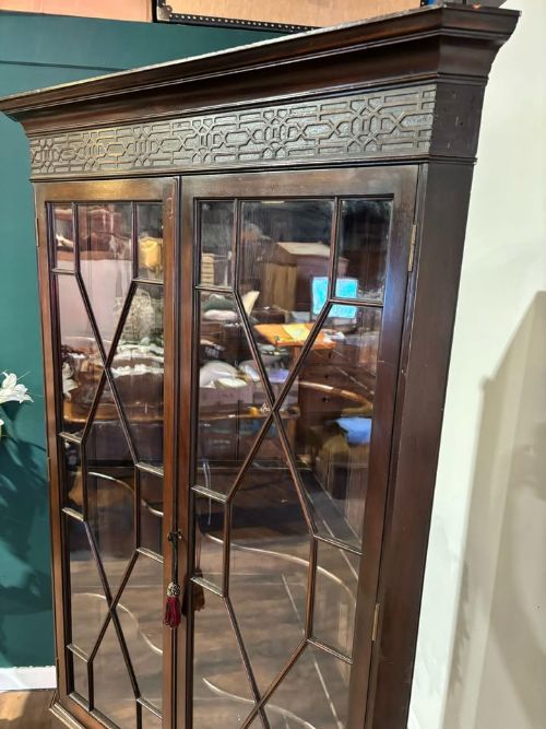 fig 5. A tall mahogany corner display cabinet featuring astragal glazed doors, a fretwork frieze, and elevated on cabriole legs.