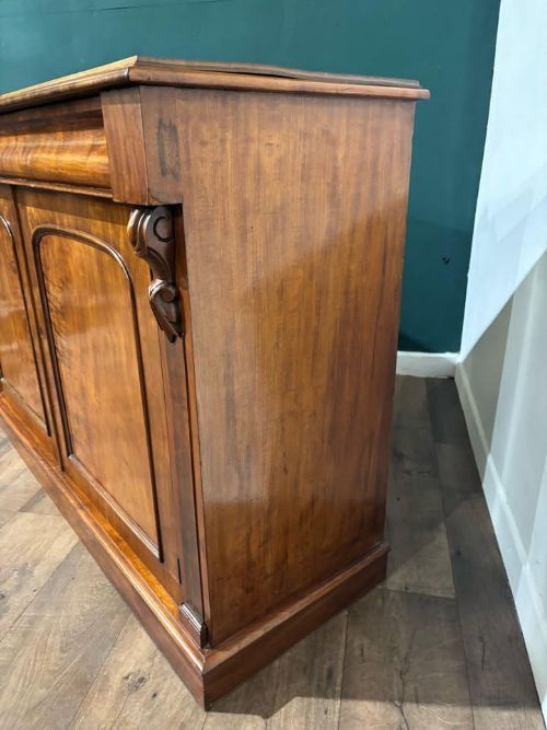 fig 1. A Victorian mahogany chiffonier featuring two flame-veneered door panels flanked by carved corbels, set beneath a frieze drawer and resting on a plinth base.