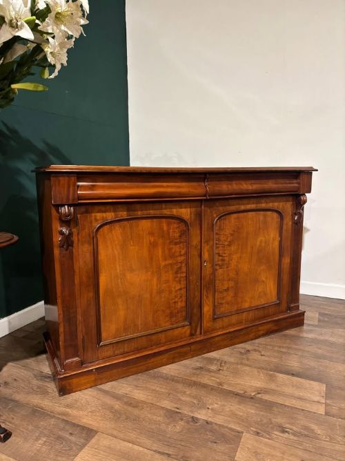 fig 2. A Victorian mahogany chiffonier featuring two flame-veneered door panels flanked by carved corbels, set beneath a frieze drawer and resting on a plinth base.