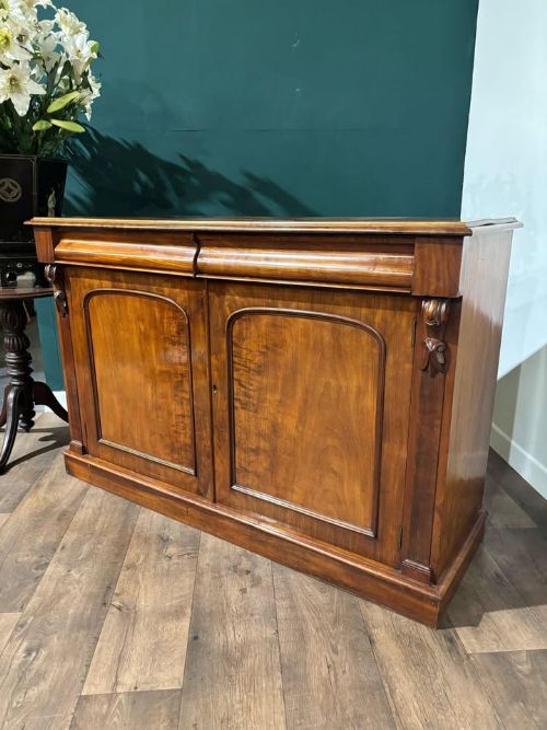 fig 5. A Victorian mahogany chiffonier featuring two flame-veneered door panels flanked by carved corbels, set beneath a frieze drawer and resting on a plinth base.