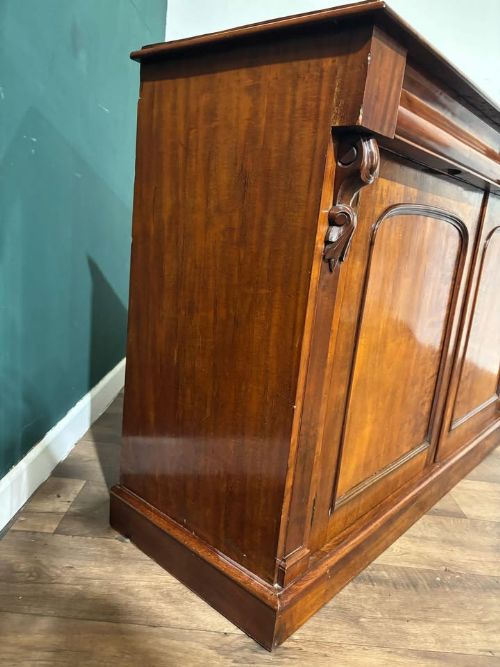 fig 6. A Victorian mahogany chiffonier featuring two flame-veneered door panels flanked by carved corbels, set beneath a frieze drawer and resting on a plinth base.