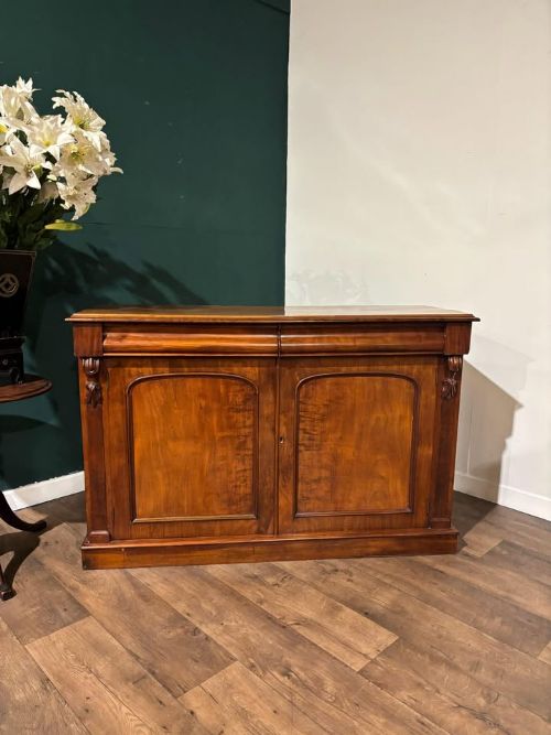 fig 7. A Victorian mahogany chiffonier featuring two flame-veneered door panels flanked by carved corbels, set beneath a frieze drawer and resting on a plinth base.