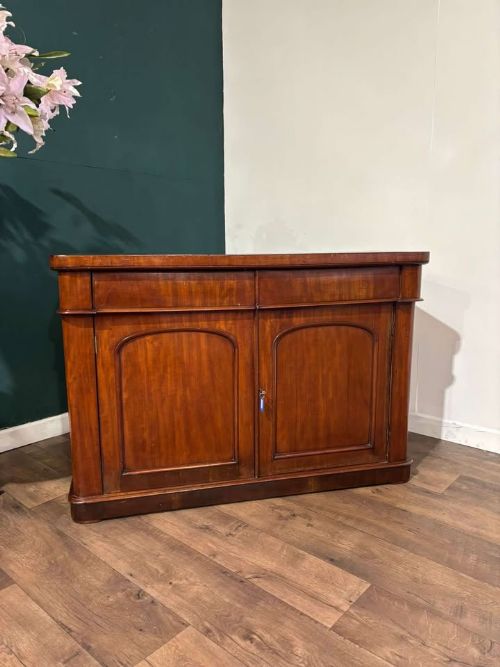 fig 1. A Victorian flame mahogany chiffonier featuring two frieze drawers set over two arched panelled cupboard doors resting on a solid plinth base.