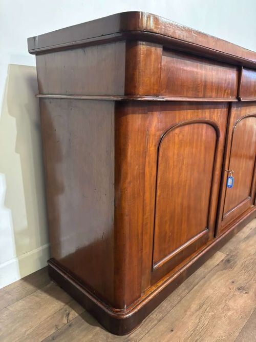 fig 3. A Victorian flame mahogany chiffonier featuring two frieze drawers set over two arched panelled cupboard doors resting on a solid plinth base.