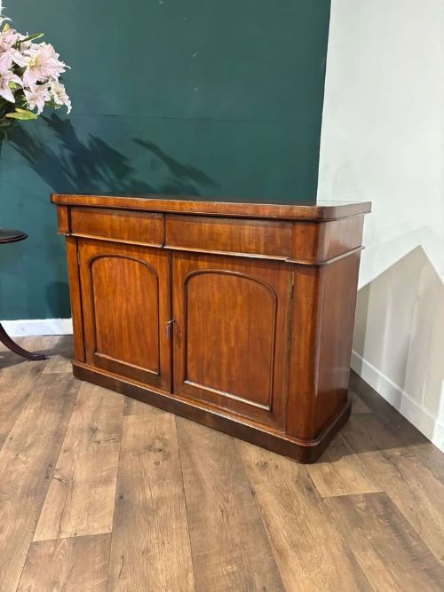 fig 4. A Victorian flame mahogany chiffonier featuring two frieze drawers set over two arched panelled cupboard doors resting on a solid plinth base.