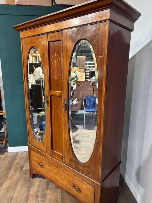 fig 2. An Edwardian walnut double wardrobe featuring two full-length oval mirrored doors flanking an inlaid central panel above a wide base drawer.