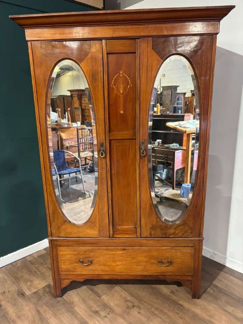 fig 8. An Edwardian walnut double wardrobe featuring two full-length oval mirrored doors flanking an inlaid central panel above a wide base drawer.