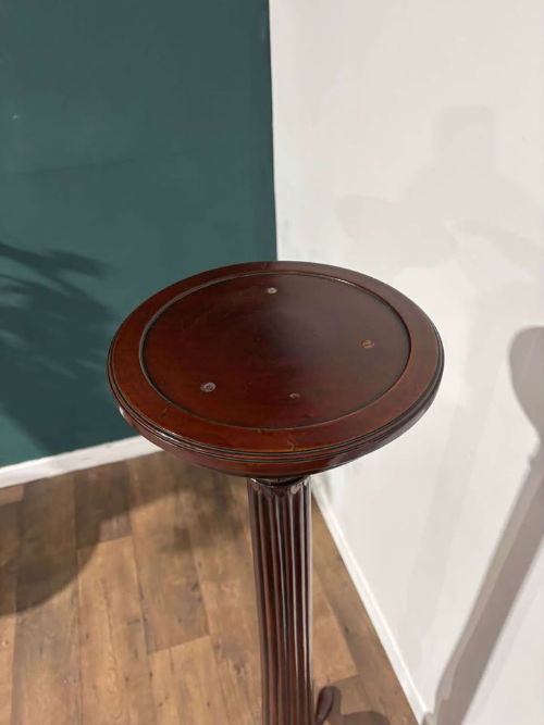 fig 3. A tall mahogany torchere plant stand featuring a circular dished top, a fluted column, and a tripod pedestal base.