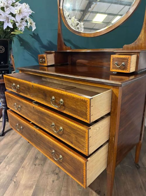 fig 1. An Edwardian mahogany dressing table featuring three long drawers with crossbanded inlay, two small upper jewellery drawers, tapered legs on castors, and a large oval swivel mirror.