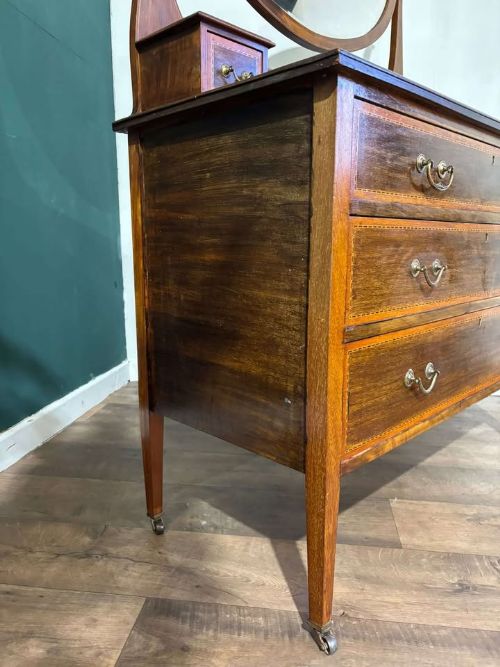 fig 3. An Edwardian mahogany dressing table featuring three long drawers with crossbanded inlay, two small upper jewellery drawers, tapered legs on castors, and a large oval swivel mirror.
