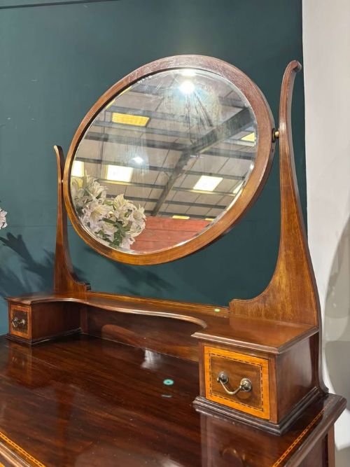 fig 8. An Edwardian mahogany dressing table featuring three long drawers with crossbanded inlay, two small upper jewellery drawers, tapered legs on castors, and a large oval swivel mirror.