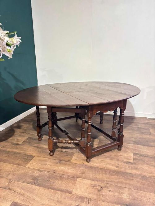 fig 3. A dark oak drop-leaf dining table with an oval top, turned legs, shaped aprons, and perimeter stretchers.
