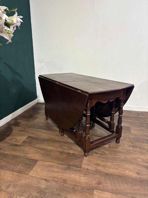 fig 6. A dark oak drop-leaf dining table with an oval top, turned legs, shaped aprons, and perimeter stretchers.