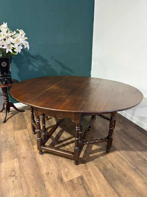 fig 7. A dark oak drop-leaf dining table with an oval top, turned legs, shaped aprons, and perimeter stretchers.