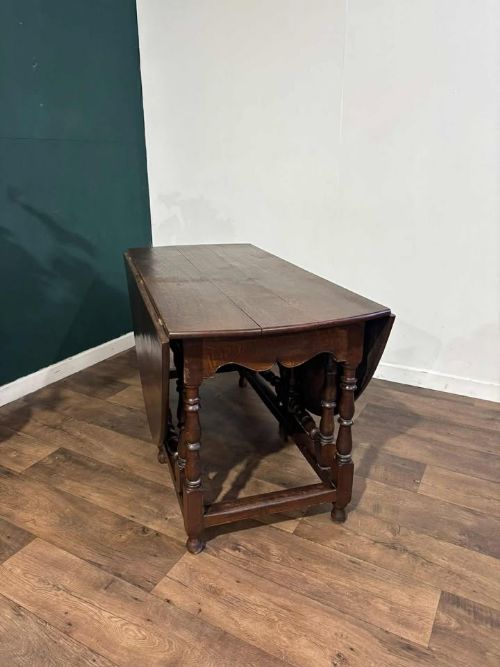 fig 8. A dark oak drop-leaf dining table with an oval top, turned legs, shaped aprons, and perimeter stretchers.