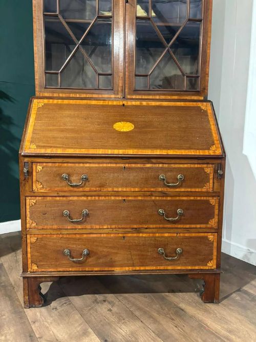 fig 1. An Edwardian mahogany bureau bookcase featuring marquetry inlay, a glazed two-door display cabinet top with a broken swan-neck pediment, a slant-front writing desk, and three long drawers below.