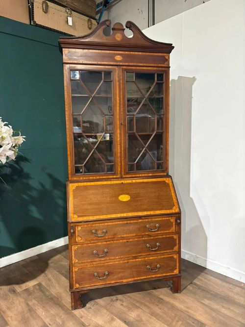 fig 2. An Edwardian mahogany bureau bookcase featuring marquetry inlay, a glazed two-door display cabinet top with a broken swan-neck pediment, a slant-front writing desk, and three long drawers below.