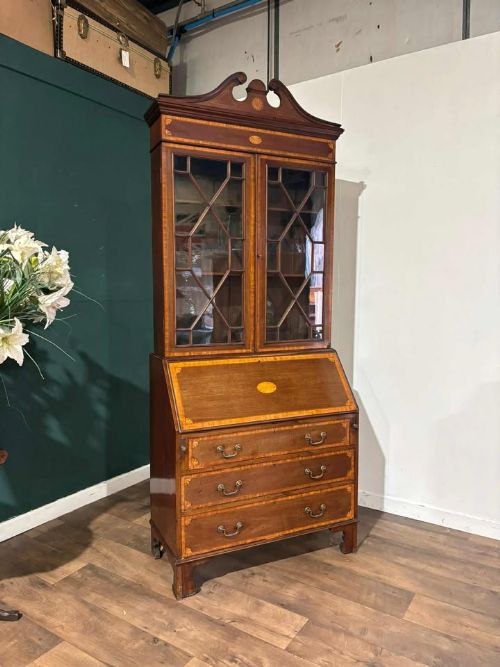 fig 3. An Edwardian mahogany bureau bookcase featuring marquetry inlay, a glazed two-door display cabinet top with a broken swan-neck pediment, a slant-front writing desk, and three long drawers below.