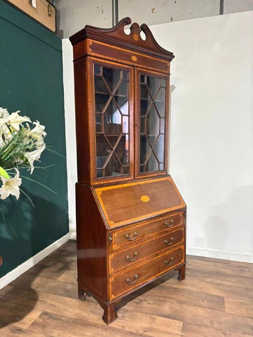 fig 4. An Edwardian mahogany bureau bookcase featuring marquetry inlay, a glazed two-door display cabinet top with a broken swan-neck pediment, a slant-front writing desk, and three long drawers below.