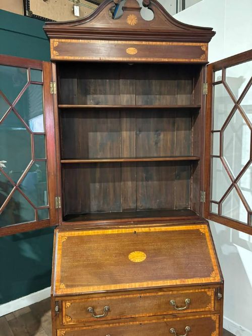 fig 5. An Edwardian mahogany bureau bookcase featuring marquetry inlay, a glazed two-door display cabinet top with a broken swan-neck pediment, a slant-front writing desk, and three long drawers below.