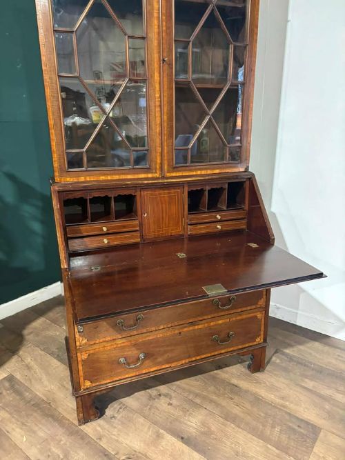 fig 6. An Edwardian mahogany bureau bookcase featuring marquetry inlay, a glazed two-door display cabinet top with a broken swan-neck pediment, a slant-front writing desk, and three long drawers below.