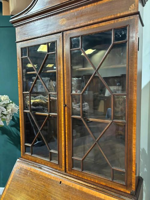 fig 7. An Edwardian mahogany bureau bookcase featuring marquetry inlay, a glazed two-door display cabinet top with a broken swan-neck pediment, a slant-front writing desk, and three long drawers below.