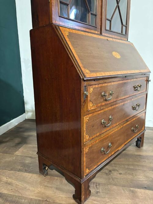 fig 8. An Edwardian mahogany bureau bookcase featuring marquetry inlay, a glazed two-door display cabinet top with a broken swan-neck pediment, a slant-front writing desk, and three long drawers below.