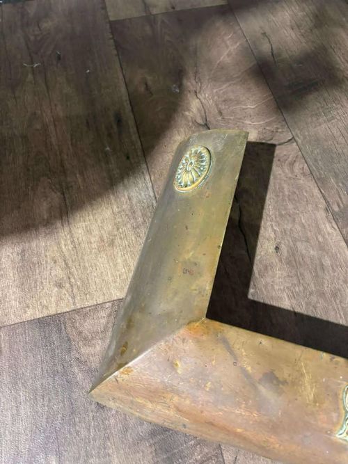 fig 3. An Edwardian brass fireplace fender featuring neoclassical swag decorative motifs on an angled metal frame.