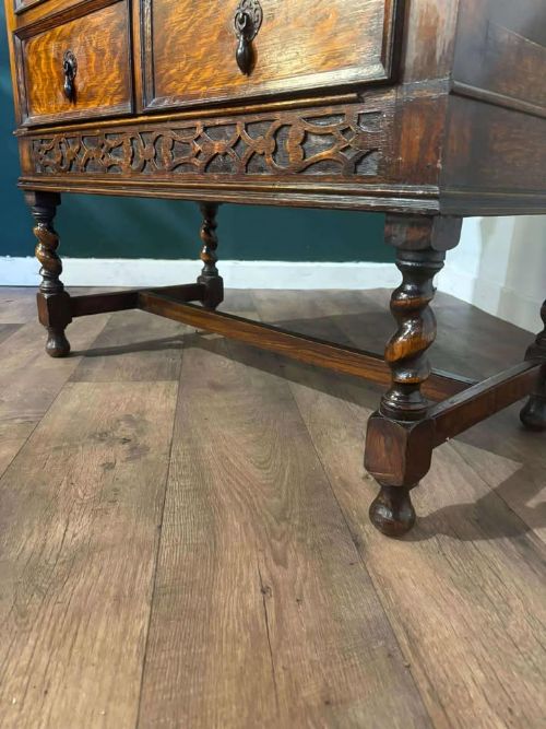 fig 2. A medium brown vintage oak chest of drawers featuring three split-panel drawer fronts, carved frieze detailing, a low back gallery, and barley twist legs connected by stretchers.