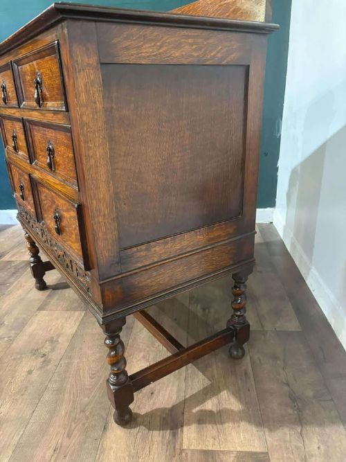 fig 4. A medium brown vintage oak chest of drawers featuring three split-panel drawer fronts, carved frieze detailing, a low back gallery, and barley twist legs connected by stretchers.
