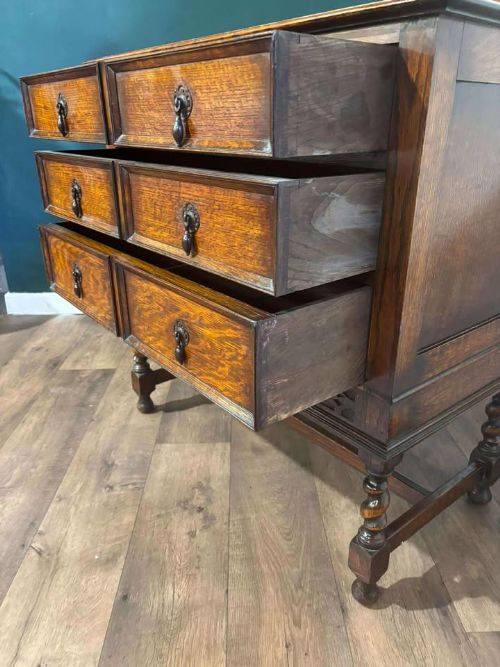 fig 5. A medium brown vintage oak chest of drawers featuring three split-panel drawer fronts, carved frieze detailing, a low back gallery, and barley twist legs connected by stretchers.