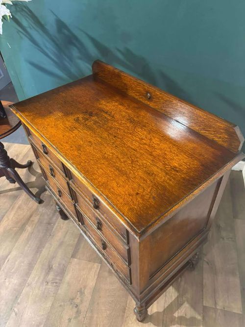 fig 7. A medium brown vintage oak chest of drawers featuring three split-panel drawer fronts, carved frieze detailing, a low back gallery, and barley twist legs connected by stretchers.