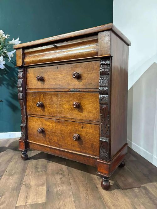 fig 1. A Victorian mahogany chest of drawers featuring carved pilasters, three main drawers with turned wooden handles, a coved top drawer, and bun feet.